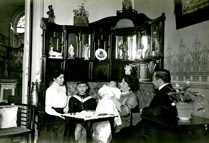 Η Μαρίκα και ο Μιχάλης Καζούλλης,  στο εσωτερικό του σπιτιού τους στην Αλεξάνδρεια, μαζί με δύο από τα παιδιά τους.  Πηγή: Αμερικανική Σχολή Κλασικών Σπουδών στην Αθήνα, Γεννάδειος Βιβλιοθήκη, Αρχείο Οικογένειας Στέφανου και Ελίζας Δραγούμη.