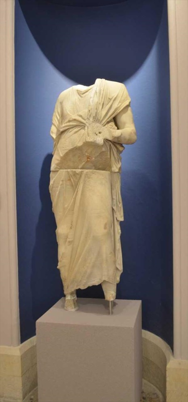 Ακέφαλο άγαλμα ανδρικής μορφής με χιτώνα και ιμάτιο. Βρέθηκε στο ρωμαϊκό Ωδείο.  Μετά το 150 π.Χ.