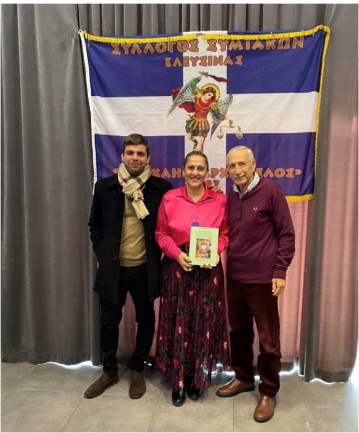 Ο κ. Χρήστος Δελαπόρτας, η κα Γεωργία Φράγκου και  ο κ. Κυριάκος Χονδρός, με φόντο  τη σημαία του Συλλόγου Συμιακών Ελευσίνας «ο Μιχαήλ Αρχάγγελος»